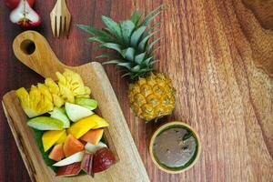 geschnitten Obst Salat, im Indonesien bekannt wie Rujak buah oder lutis oder Lotis. serviert mit würzig braun Zucker Soße und Boden Erdnüsse im ein Teller auf Holz Hintergrund foto