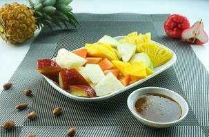 geschnitten Obst Salat, im Indonesien bekannt wie Rujak buah oder lutis oder Lotis. serviert mit würzig braun Zucker Soße und Boden Erdnüsse im ein Teller auf Weiß Hintergrund foto