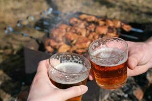 freunde Klirren Bier während entspannend draußen mit Grill im das Hintergrund foto