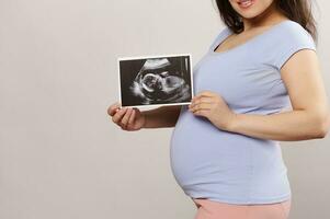 Nahansicht Bauch von ein lächelnd schwanger Frau halten Ultraschall Scan Bild Über isoliert Hintergrund. Schwangerschaft. Geburt foto