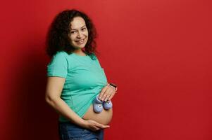 glücklich schwanger Frau Putten süß gestrickt Baby Socken zum ihr Neugeborene Junge auf ihr nackt Bauch, lächelnd suchen beim Kamera foto