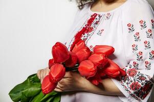 Einzelheiten auf ein Strauß von rot Tulpen im das Hände von ein Frau, gekleidet im ukrainisch traditionell gestickt Kleid foto