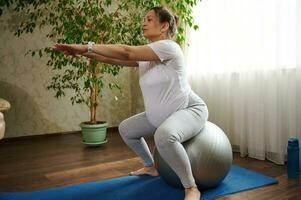 aktiv Erwachsene schwanger Frau ausüben mit passen Ball beim heim. vorgeburtlich Fitness zum gesund Schwangerschaft und einfach Geburt foto