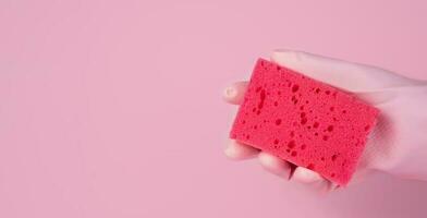 ein Frau Hand im ein Gummi Handschuh hält ein Reinigung Schwamm auf ein Rosa Hintergrund. Waschen und Reinigung Konzept. Nahansicht. Kopieren Raum. Banner. selektiv Fokus. foto