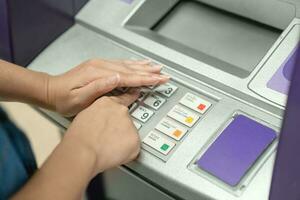 Frau Abdeckung ihr Hände während eintreten ihr Stift beim ein Geldautomat foto