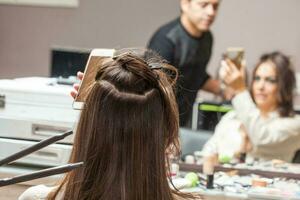 Stylist mit eben Eisen auf Haar von weiblich Klient Sitzung im Salon Stuhl foto