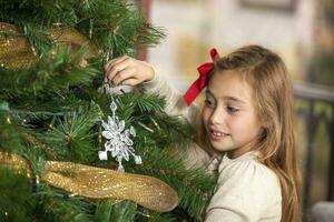 ein blond Mädchen dekorieren das Weihnachten Baum foto