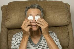 Senior Mann im das Badezimmer mit Baumwolle Pads zum Auge Linderung foto