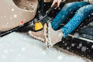 Frau im Winter im schwer Schnee Bürsten Schuhe von Schnee Vor bekommen in das Auto - - Auto Pflege foto