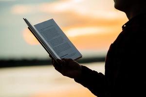asiatischer Mann, der Buch mit Sonnenuntergang liest foto