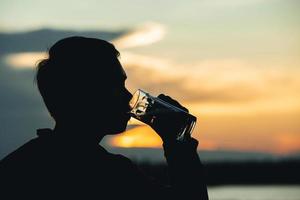 Schattenbildmann, der Glasbier mit Sonnenunterganghintergrund hält foto