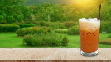 vereist thailändisch Milch Tee im Glas, Milch Eis Tee, Cheddar ist ein traditionell thailändisch trinken auf hölzern Tabelle mit Natur Hintergrund, Sommer- Getränke mit vereist foto