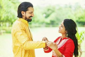 jung indisch Frau binden Rakhi auf ihr Brüder Hand zu feiern Raksha Bandhan foto