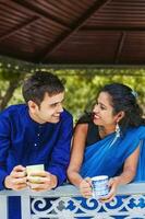 schön indisch Paar tragen traditionell Kleider Trinken Kaffee oder Tee auf ein Balkon und reden foto