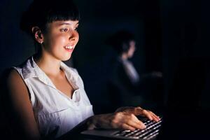 kaukasisch Frau Arbeiten auf Laptop im Dunkelheit foto