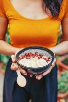 gesichtslos Foto von ein Frau halten acai Smoothie Schüssel mit Granatapfel und hölzern Löffel