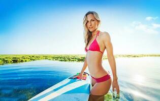 sexy Surfer Mädchen posieren mit das Surfen Tafel im das Ozean, bali foto