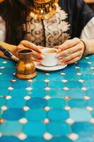 Nahansicht Foto von Frau halten ein Tasse von Türkisch Kaffee im ein Cafe mit Türkis Fliesen Tabelle