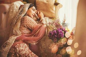 Herrlich Jahrgang Stil indisch Braut Sitzung im ein Luxus Hotel Zimmer tragen traditionell Lehenga mit ghungat foto
