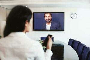 jung indisch Frau tun Video Konferenz mit Direktor von ihr Unternehmen online auf ein groß Bildschirm Fernseher foto