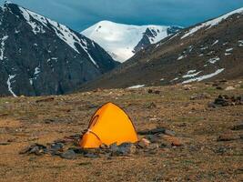Solo Trekking. Camping auf ein felsig Hohe Höhe Plateau. Gelb Zelt auf das Hintergrund von Gletscher und hoch schneebedeckt Berge. foto