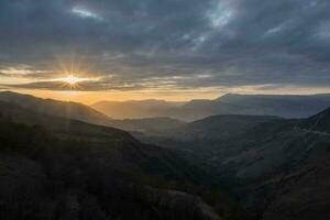 zuletzt Strahlen von das Rahmen Sonne Über ein bergig Plateau. golden Sonnenuntergang im Berg Landschaft. Silhouette von das Abend Berge beim Sonnenuntergang. matlas Senke beim Sonnenuntergang im Dagestan. foto