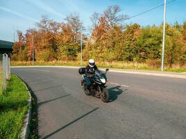 Motorradfahrer im Bewegung. Frau Biker auf ein schwarz Motorrad im der Verkehr auf ein ländlich Herbst Straße foto