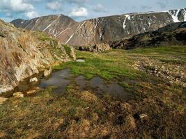 beeindruckend Landschaft mit Pfützen auf ein steinig Wiese und riesig Berge im Sonnenlicht. nass Berg Wiese. foto