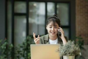 jung asiatisch Geschäftsfrau Arbeiten beim Büro mit Handy, Mobiltelefon Telefon. foto