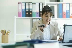 jung asiatisch Geschäftsfrau ist Arbeiten beim Büro mit Handy, Mobiltelefon Telefon. foto