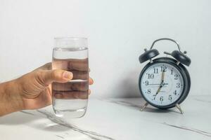 männlich Hand halten ein Glas von Wasser Hintergrund Uhr foto