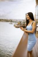 junge Frau, die ein Mobiltelefon benutzt, während sie auf der Flusspromenade steht