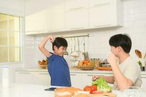 asiatisch Junge zeigen stark Arm , spielerisch mit seine Vater im Zuhause foto