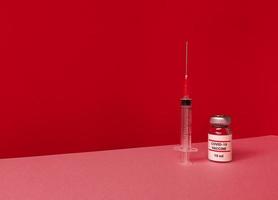 Medizinische Flasche mit Covid 19-Impfstoff und Spritze auf rotem Hintergrund mit geneigter trendiger Skyline und Kopierraum