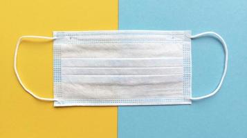 medizinische Gesichtsmaske auf gelbem und blauem Hintergrund einfaches flaches medizinisches Konzeptvorratfoto