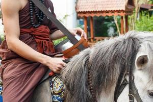 buddhistischer Mönch mit braunem Gewand reitet Pferd und bittet um Almosen, die in Thailand im wilden Höhlengold-Pferdetempel in Chiangrai Thailand unsichtbar sind foto