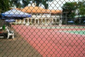 Metall Gittergewebe auf ein verschwommen Hintergrund von ein Tennis Gericht mit Spieler. foto