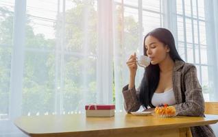 schöne Frau sitzt, um Brot und Morgencafé im Urlaub zu essen und das Licht scheint von außen foto