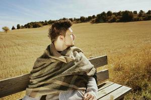 Seitengesicht eines sitzenden jungen Mannes mit geschlossenen Augen, der in Ruhe die morgendliche Herbstsonne in einem gelben Feld genießt