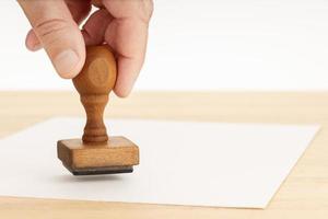 Hand hält einen Stempel und leeres Papier auf Holztisch