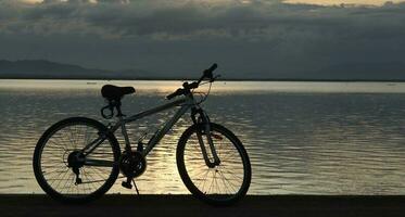 Silhouette von ein Fahrrad gegen das Hintergrund von das Sonnenuntergang auf das See foto