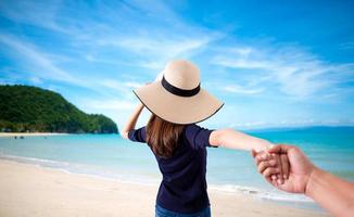 Frau, die Hand ihres Mannes hält, während sie zusammen am Strand laufen foto