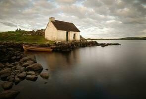 schön Morgen Seeufer Szene von Fischers Hütte und hölzern Boot reflektiert im See beim Geröll, connemara National Park im Bezirk Galway, Irland foto