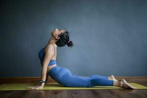 asiatisch Frau tun Yoga Pose im Zuhause Leben Zuhause gegen leeren grau Mauer foto