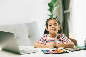 wenig asiatisch Mädchen Zeichnung mit Farbe Bleistifte und Laptop beim Zuhause foto