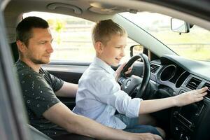 Papa und glücklich Sohn im das Vorderseite Sitz von ein Auto Fahren ein Wagen. das Junge hält das Lenkung Rad. foto