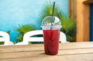 rot Saft im ein Plastik Glas mit ein Stroh ist auf das Tabelle im ein Strand Cafe foto