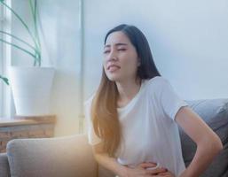 Schöne asiatische Frauen sitzen auf der Couch. Sie hat Magenkrämpfe aufgrund der Menstruation foto