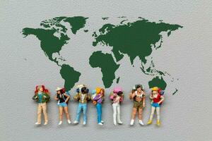 Miniatur Menschen Stehen auf das Welt Karte mit grau Hintergrund foto