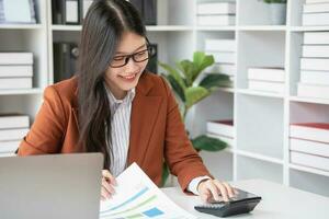 Geschäftsfrau Arbeiten im das Büro mit Taschenrechner zu Berechnung finanziell Berichte. Der Umsatz Daten mit Laptop Computer und Geschäft Unterlagen auf Büro Tisch. schließen hoch. Geschäft Finanzen und Investition. foto